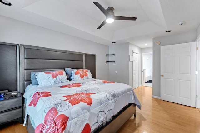 bedroom featuring ceiling fan, a tray ceiling, ensuite bathroom, and light hardwood / wood-style flooring