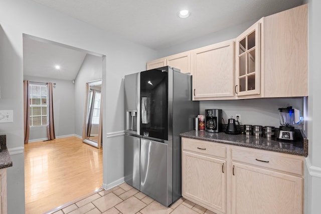 kitchen featuring stainless steel fridge, dark stone countertops, vaulted ceiling, light brown cabinets, and light hardwood / wood-style flooring