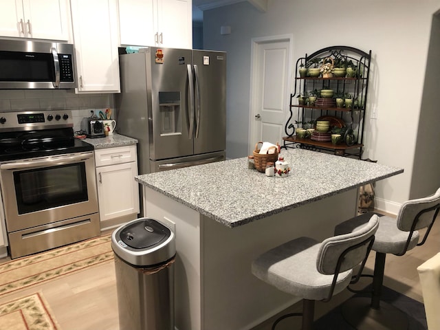 kitchen with decorative backsplash, white cabinetry, stainless steel appliances, and a breakfast bar