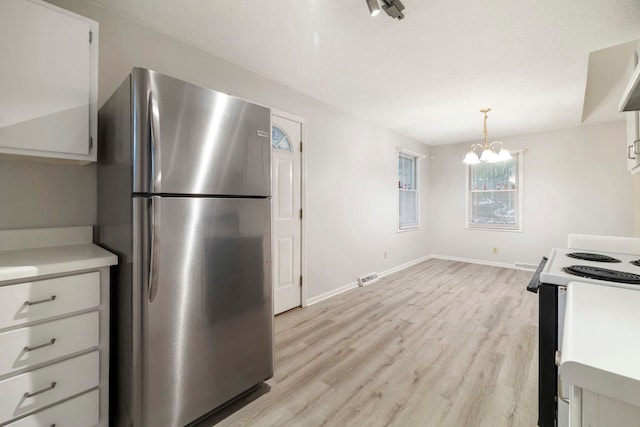 kitchen with electric stove, white cabinetry, hanging light fixtures, stainless steel refrigerator, and an inviting chandelier