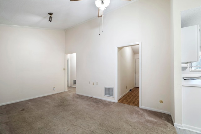 carpeted empty room featuring ceiling fan, ornamental molding, and a high ceiling