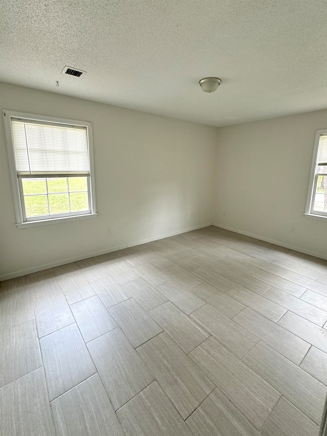 empty room with light wood-type flooring and a textured ceiling