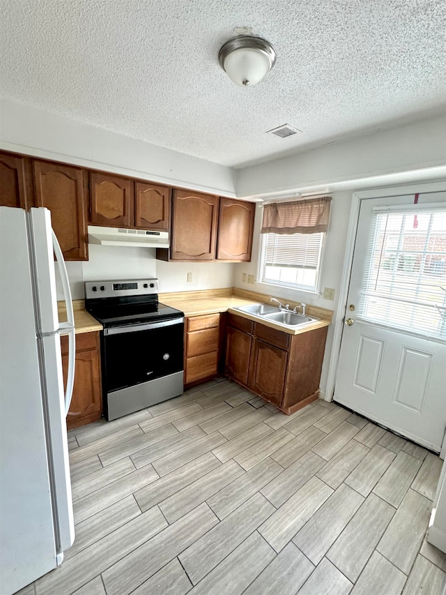 kitchen with light wood-type flooring, white refrigerator, a textured ceiling, sink, and stainless steel electric stove