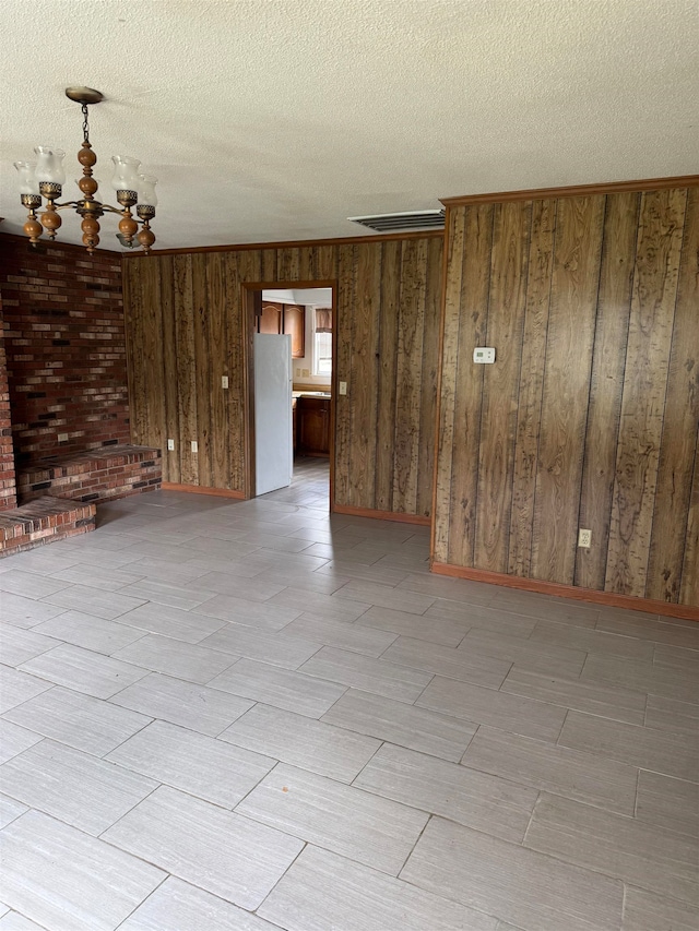 unfurnished room with a notable chandelier, wooden walls, and a textured ceiling