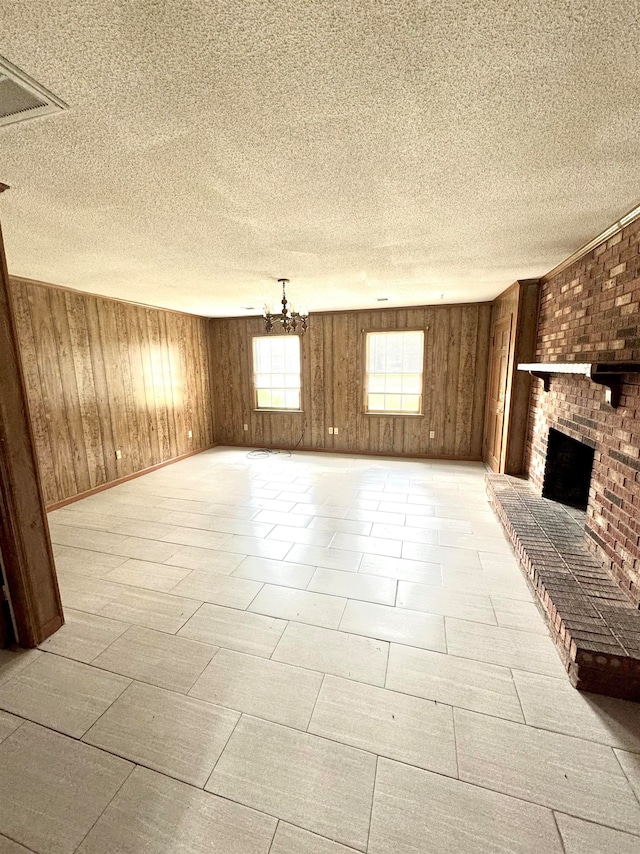 unfurnished living room with a brick fireplace, a chandelier, a textured ceiling, and wooden walls