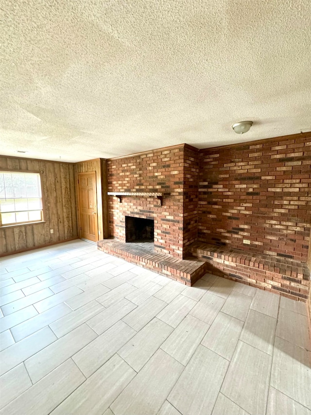 unfurnished living room with brick wall, a fireplace, a textured ceiling, light wood-type flooring, and wooden walls