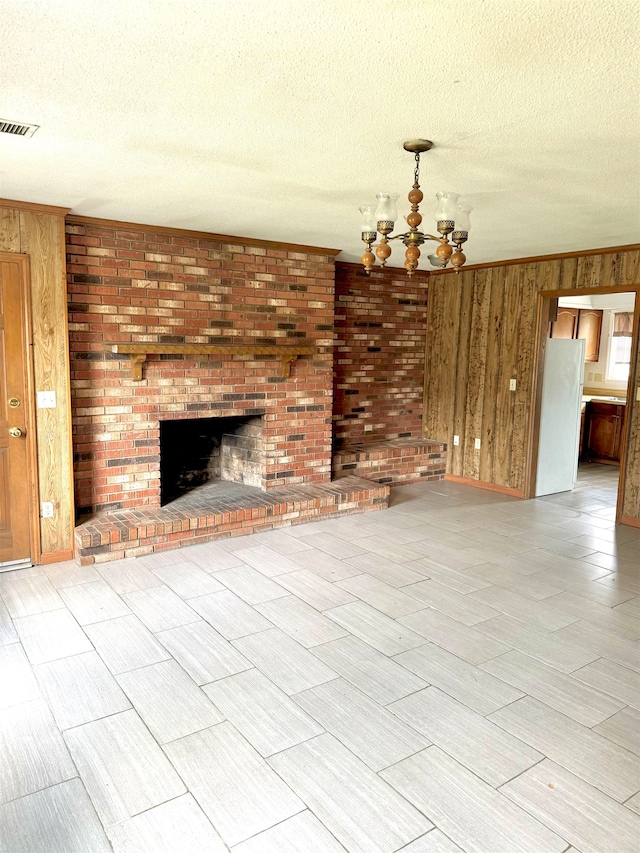 unfurnished living room featuring a notable chandelier, a fireplace, wooden walls, and a textured ceiling