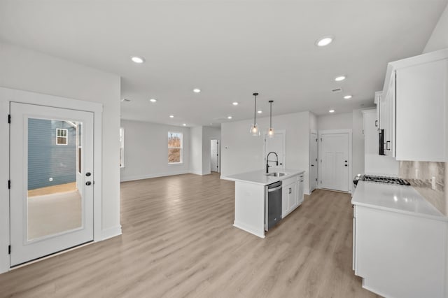 kitchen with stainless steel dishwasher, pendant lighting, sink, white cabinetry, and a center island with sink