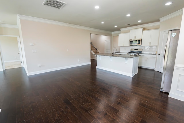 kitchen with white cabinets, stainless steel appliances, an island with sink, decorative backsplash, and a kitchen breakfast bar