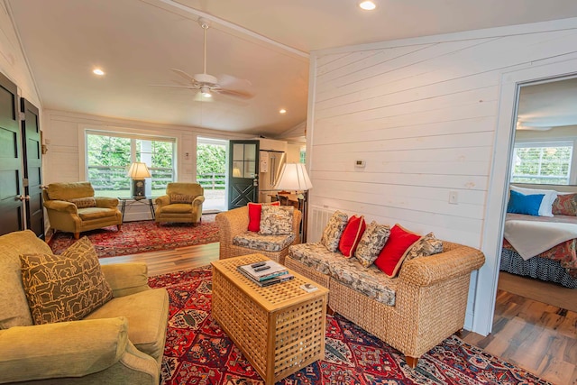 living room featuring wooden walls, wood-type flooring, vaulted ceiling, and ceiling fan