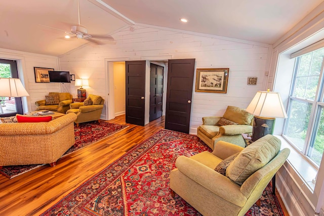 living room with lofted ceiling, wooden walls, hardwood / wood-style floors, and ceiling fan