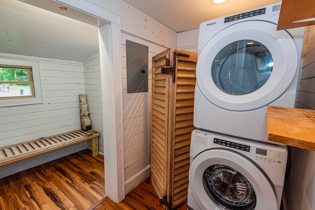 washroom featuring wooden walls, electric panel, hardwood / wood-style floors, and stacked washing maching and dryer