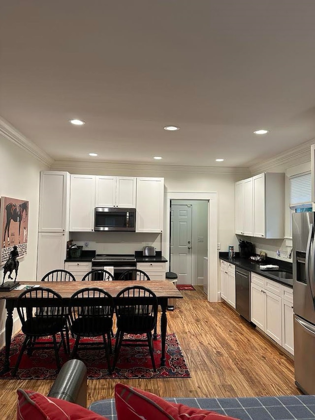 kitchen with light hardwood / wood-style flooring, white cabinets, appliances with stainless steel finishes, and crown molding