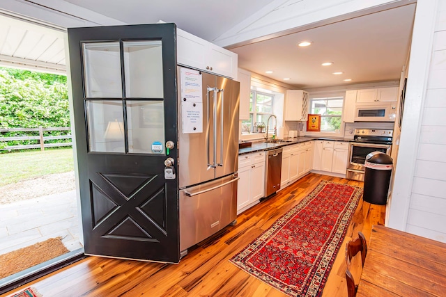 kitchen featuring white cabinetry, stainless steel appliances, lofted ceiling, hardwood / wood-style floors, and sink