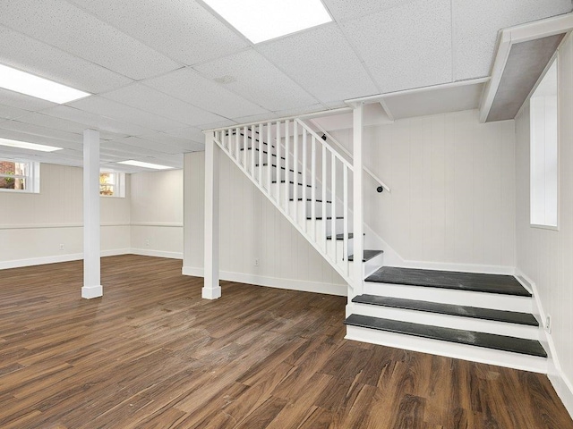 basement with wooden walls, a drop ceiling, and dark hardwood / wood-style floors