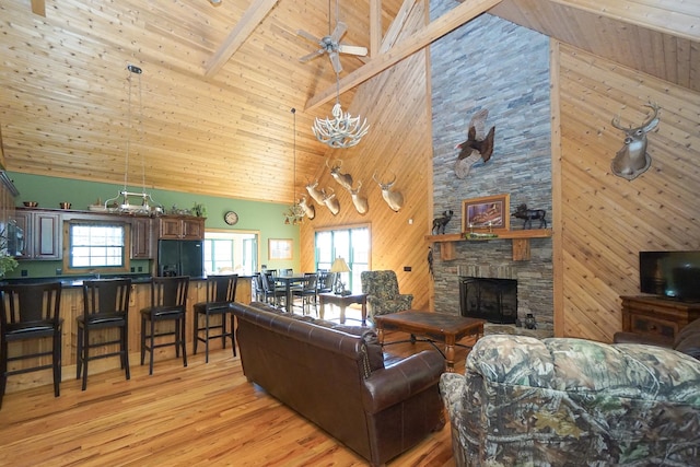 living room with high vaulted ceiling, a wealth of natural light, beamed ceiling, and a stone fireplace