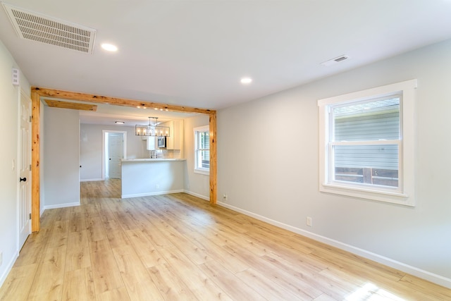 unfurnished living room with an inviting chandelier and light wood-type flooring