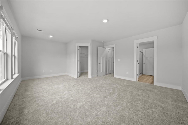 unfurnished bedroom featuring ensuite bathroom, light carpet, a walk in closet, and a closet