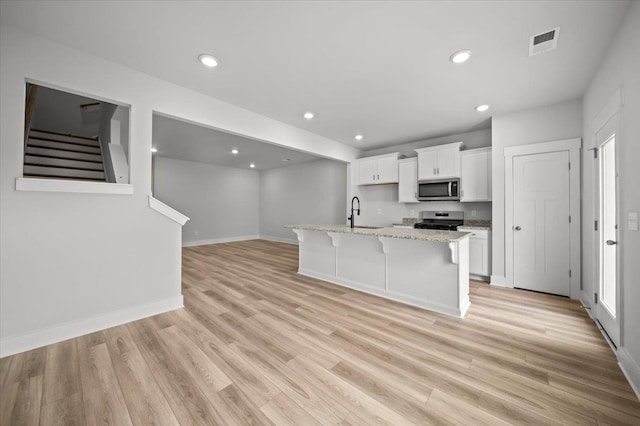 kitchen with appliances with stainless steel finishes, a center island with sink, white cabinetry, and light hardwood / wood-style flooring