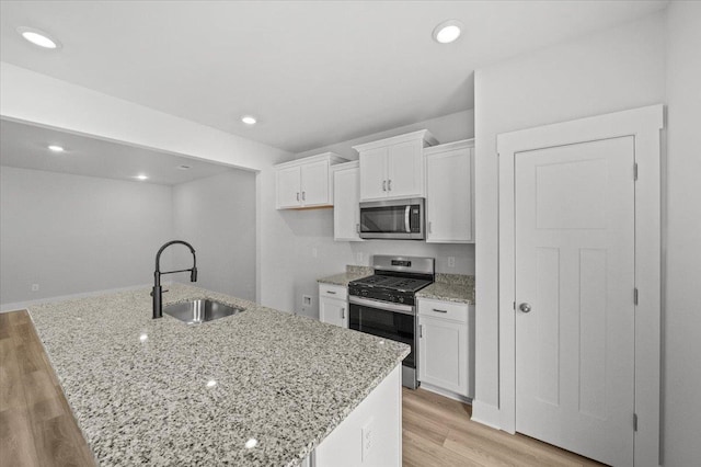 kitchen featuring sink, a center island with sink, white cabinetry, stainless steel appliances, and light hardwood / wood-style floors