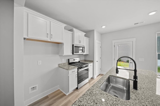 kitchen featuring light stone counters, sink, white cabinetry, light hardwood / wood-style flooring, and appliances with stainless steel finishes