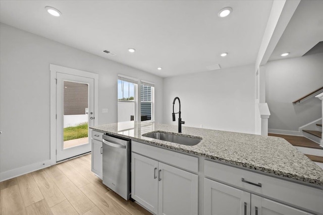 kitchen with light wood-type flooring, light stone counters, sink, white cabinets, and stainless steel dishwasher