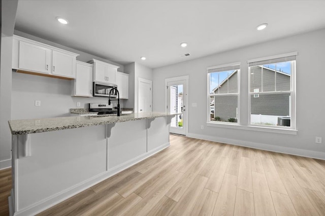 kitchen featuring light wood-type flooring, appliances with stainless steel finishes, plenty of natural light, and white cabinetry