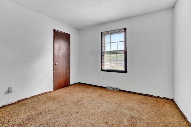 empty room with light colored carpet and a textured ceiling