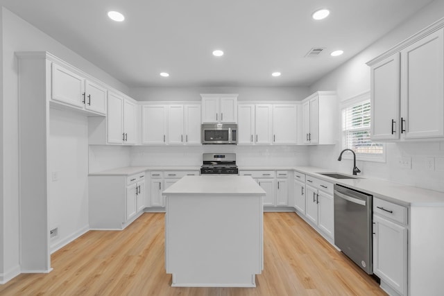 kitchen featuring light wood-type flooring, a center island, white cabinets, sink, and appliances with stainless steel finishes