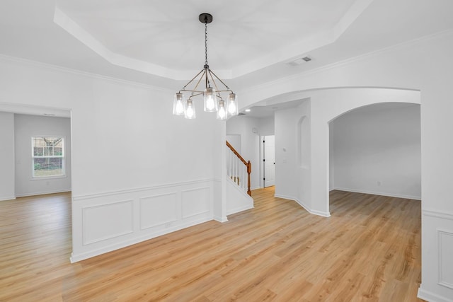 empty room featuring crown molding, an inviting chandelier, light hardwood / wood-style floors, and a raised ceiling