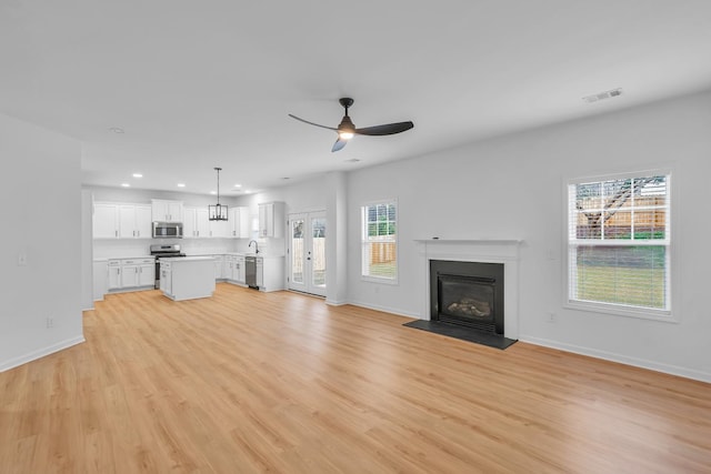 unfurnished living room featuring a healthy amount of sunlight, ceiling fan, sink, and light hardwood / wood-style flooring