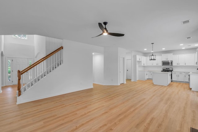 unfurnished living room featuring ceiling fan with notable chandelier, light wood-type flooring, and plenty of natural light