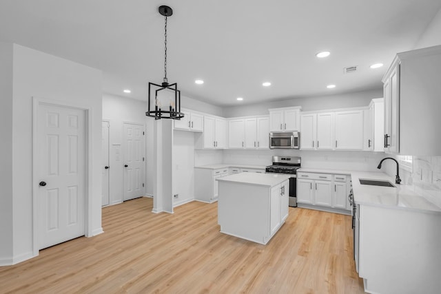 kitchen with light wood-type flooring, a kitchen island, sink, white cabinets, and appliances with stainless steel finishes