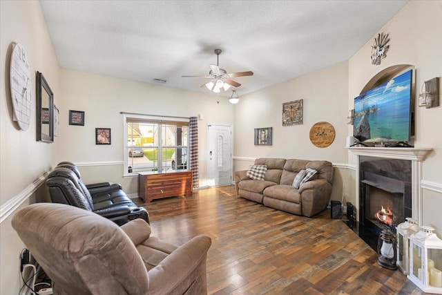 living room featuring ceiling fan, a textured ceiling, a fireplace, and dark hardwood / wood-style flooring