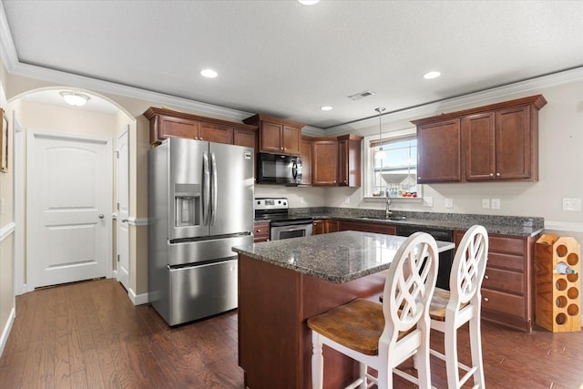 kitchen featuring ornamental molding, a kitchen island, decorative light fixtures, dark wood-type flooring, and stainless steel appliances