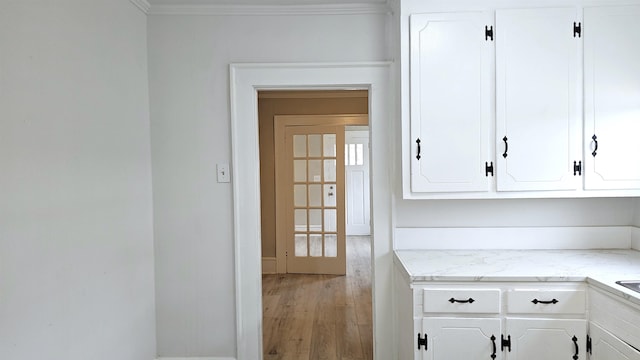 kitchen with light stone countertops, crown molding, white cabinets, and light hardwood / wood-style flooring