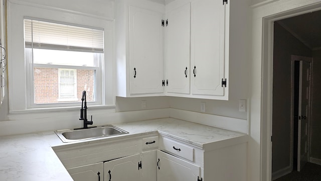 kitchen featuring light stone counters, white cabinets, and sink