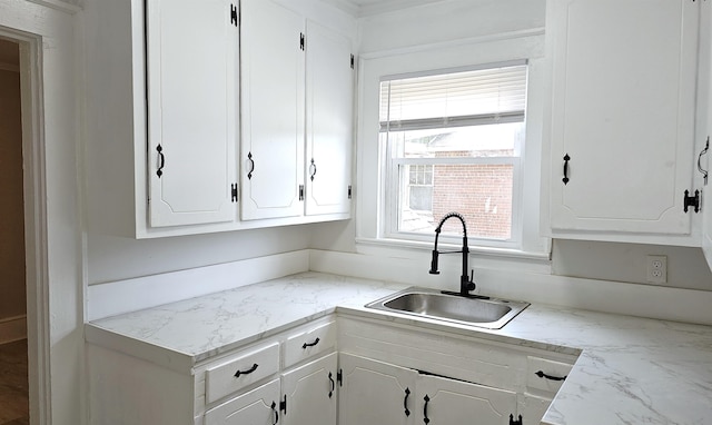 kitchen with light stone countertops, sink, and white cabinetry