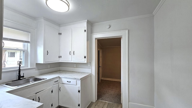 kitchen with white cabinets, light hardwood / wood-style floors, crown molding, and sink