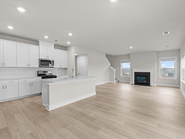 kitchen with stainless steel appliances, white cabinetry, a kitchen island with sink, and a healthy amount of sunlight