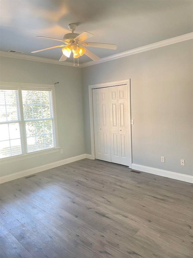 unfurnished bedroom with crown molding, hardwood / wood-style flooring, a closet, and ceiling fan