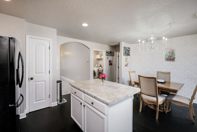 kitchen featuring black fridge, independent washer and dryer, a center island, white cabinets, and a textured ceiling