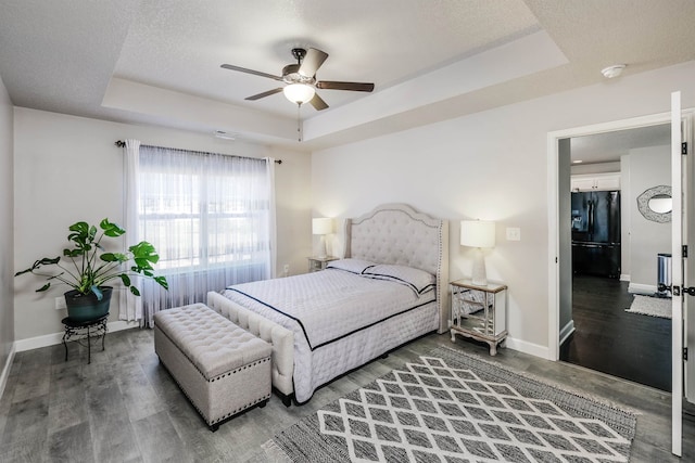 bedroom featuring dark wood-type flooring, ceiling fan, a raised ceiling, and black refrigerator with ice dispenser