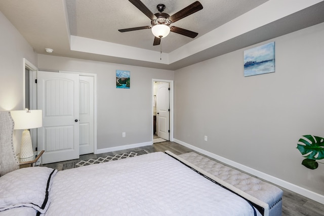 bedroom with a closet, ceiling fan, a raised ceiling, and dark hardwood / wood-style flooring