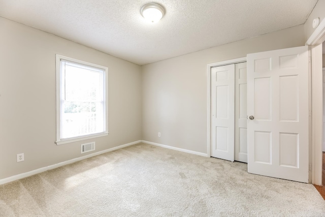 unfurnished bedroom with a closet, a textured ceiling, and light colored carpet