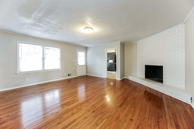 unfurnished living room with ornamental molding, hardwood / wood-style floors, a brick fireplace, and a textured ceiling