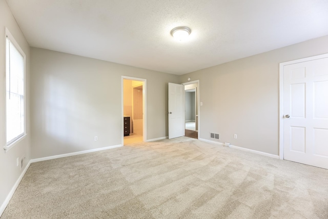 unfurnished bedroom with light carpet, multiple windows, and connected bathroom