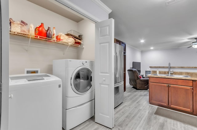 clothes washing area featuring light hardwood / wood-style flooring, crown molding, sink, washing machine and clothes dryer, and ceiling fan