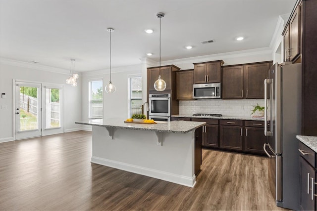 kitchen with appliances with stainless steel finishes, dark hardwood / wood-style flooring, a center island with sink, and a kitchen breakfast bar