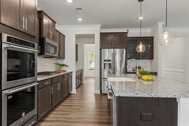 kitchen featuring hardwood / wood-style floors, hanging light fixtures, an island with sink, appliances with stainless steel finishes, and dark brown cabinetry